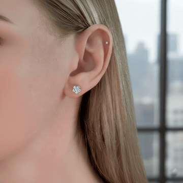 Close-up of a person wearing diamond stud earrings with a blurred cityscape background